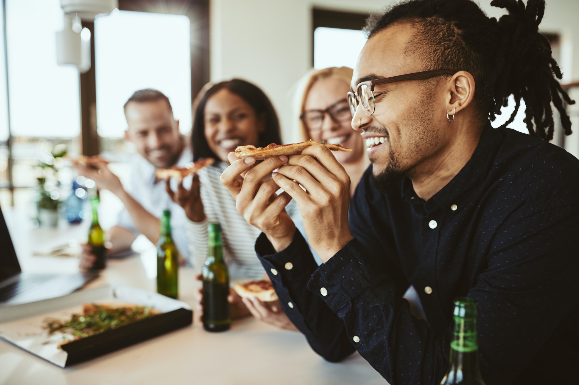 Laughing African American businessman having beers and pizza with coworkers